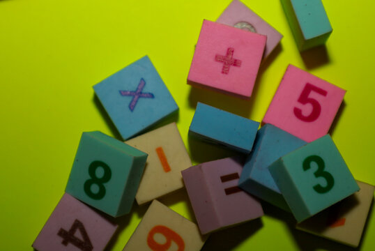 This photograph captures a random scatter of multi-colored blocks or tiles featuring embossed numbers and mathematical symbols on a vibrant lime-green background.