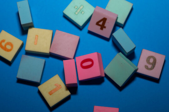 This close-up shot features a random scatter of multi-colored square tiles with embossed numbers and a mathematical symbol set against a bright blue background.