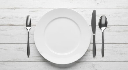 Empty white plate with silverware on distressed white wooden table.