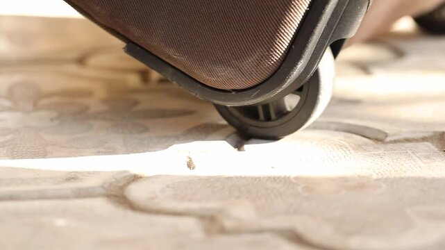Extreme close-up of a brown luggage wheel rolling slowly across decorative, sunlit outdoor paving. This shot represents the themes of travel, journey, and movement.