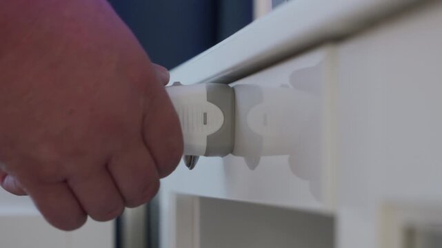 Hand holding white plastic key to open a white cabinet drawer secured by a child safety lock. The magnetic lock is activated and the drawer is pulled open.