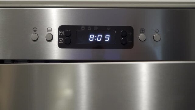 Hand pressing the buttons on the stainless steel control panel of a microwave oven. The button presses set the cooking time. The action results in soft electronic beeps and light plastic clicking.