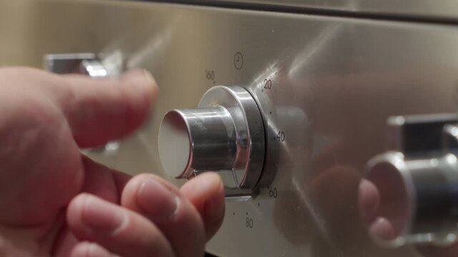 Hand turning a silver metallic control knob on a stainless steel oven. The knob rotates to set the timer. A repetitive, distinct, and metallic clicking sound is produced.