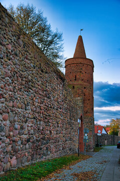 Fototapeta Strzelce Krajeńskie – Wieża Więzienna – Zabytkowa wieża z czerwonej cegły z kamiennym murem o zmierzchu pod błękitnym niebem.