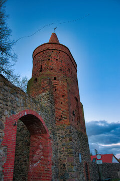 Fototapeta Strzelce Krajeńskie – Wieża Więzienna – Zabytkowa wieża z czerwonej cegły z kamiennym łukiem bramnym o zmierzchu pod błękitnym niebem.