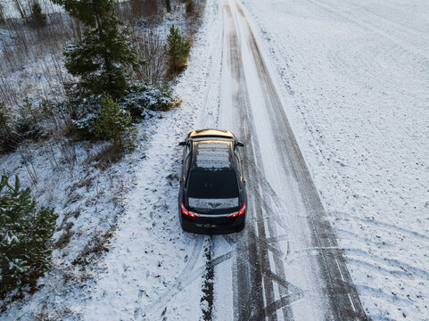 Aerial drone view of a black car on a slippery, snowy country road in the rural Estonian winter landscape.