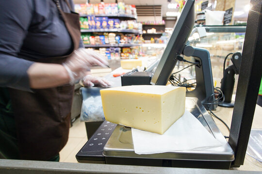 A salesperson placed a piece of cheese on a scale and was calculating its price. A large piece of cheese was lying on the scale in a store.