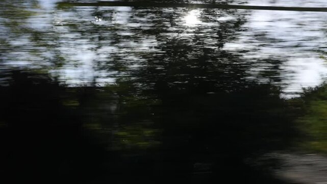 View from a fast-moving car showing the blurred rural landscape, fields, and trees through the side window and dirty mirror. Motion blur travel concept.