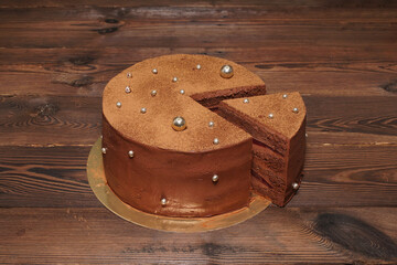 A confection. A chocolate cake with a cut-out piece on a golden base, on a wooden table.