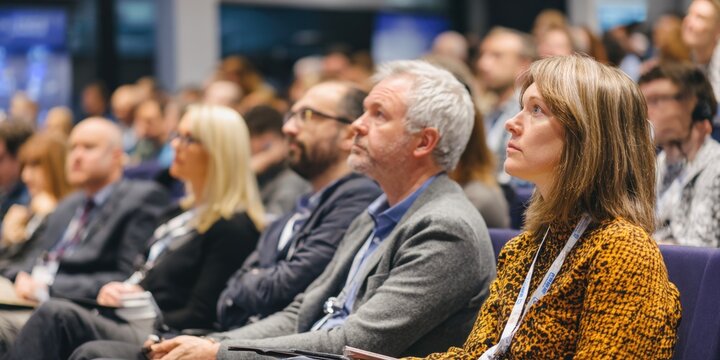 group of professional adults sitting intently in audience, listening to speaker at corporate conference, seminar, or academic event. Captures focus, learning, and engagement at large business meeting - Powered by Adobe