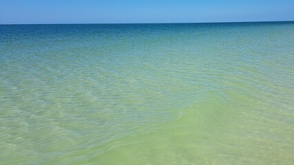Scenic view of clear ocean water, sharp straight horizon line and blue sky.