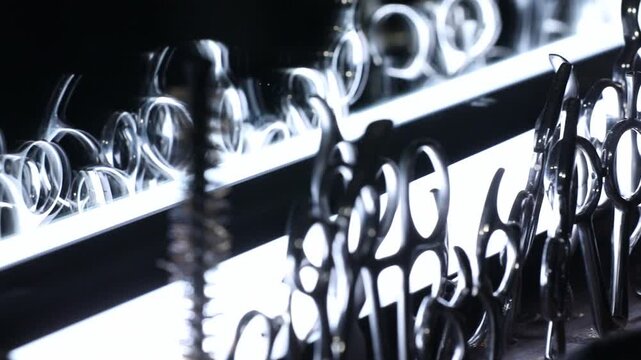 Professional barber scissors and shears stand organized in a backlit display. Dramatic lighting highlights the shiny metal tools used for precision haircutting in a modern salon or barbershop.