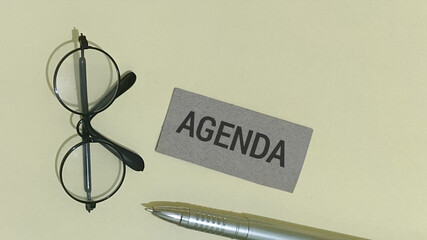 Flat lay of a professional workspace with an agenda card, classic eyeglasses, and a silver pen, representing strategic business planning