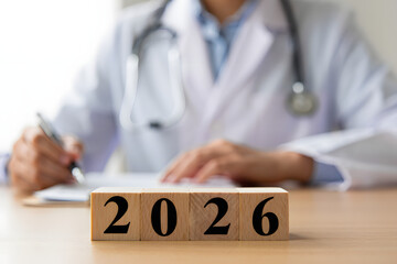 Medical forecast in 2026: A focused doctor, with a stethoscope draped around the neck, writes diligently, a wooden block displays the year 2026, creating a sense of anticipation and future planning.