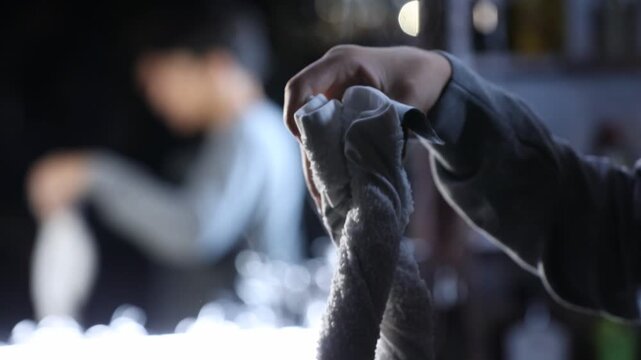 Silhouette of a barber's hand holding a hot, steaming towel in a dark, atmospheric setting. Traditional grooming ritual preparation for a luxurious shave or facial treatment.