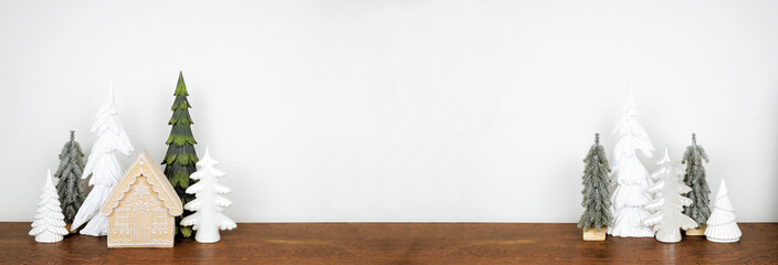 Green and white Christmas tree and gingerbread house decor on a wood shelf against a white wall banner background with copy space