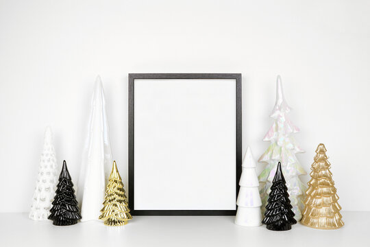 Christmas mock up with black wooden frame and gold, black and white Christmas tree decor. Portrait frame on a white shelf against a white wall. Copy space.