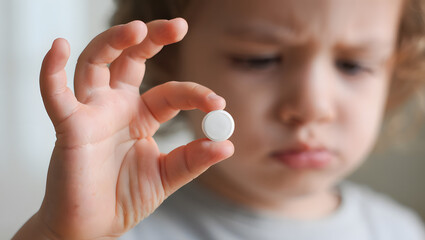 Uncertain Remedy: A child's apprehensive gaze meets a small, white tablet held delicately between fingers, hinting at the difficult choice between health and hesitation. 