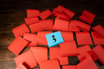Single semi colon on blue sticky note in a grid pattern of red sticky notes on top of dark wood surface.  Your story isn't over.