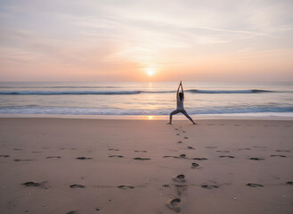 woman practicing yoga pose during sunrise on sandy coastline