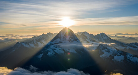 Majestic snow capped mountain peak illuminated by a brilliant sunrise casting long shadows over a sea of clouds below