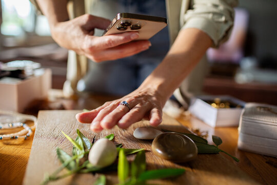 Adult woman arranging and photographing spa stones at home, focused