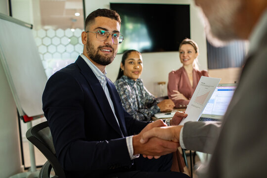 Young adults closing a deal at business meeting in modern office, confident