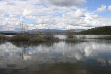 Fototapeta premium The calm waters of the Aguilar reservoir reflect the clouds and distant hills - Aguilar de Campoo