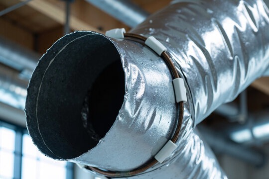 Close-up industrial metallic silver flexible aluminum ventilation air duct pipe with black circular outlet opening, HVAC system component for climate control and airflow distribution in buildings