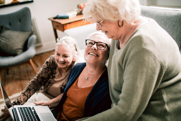 Senior female friends laughing with laptop at home