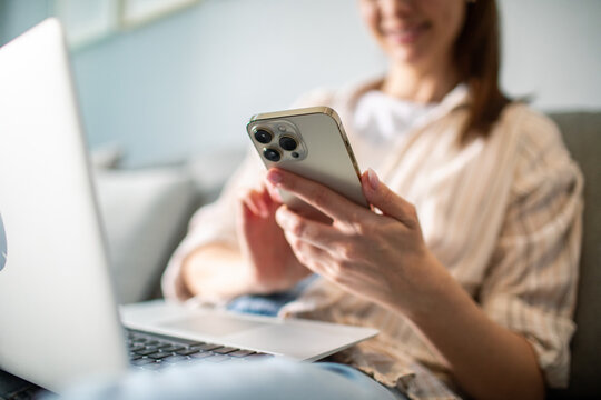 Young adult woman smiling using smartphone and laptop at home