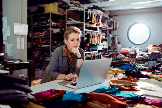 Adult woman focused working on laptop in textile studio