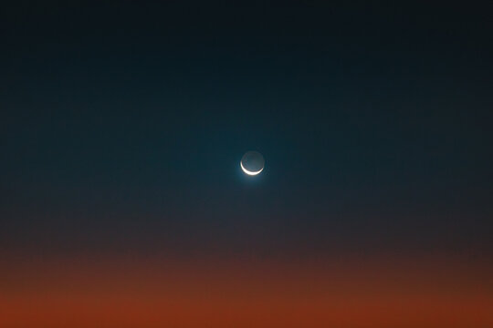 Sliver of moon over a sunrise gradient