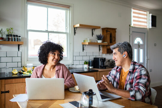 Adult couple collaborating on laptops in home kitchen, cheerful