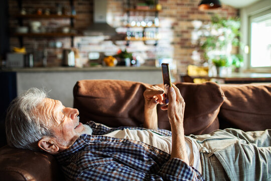 Senior man smiling while using smartphone on sofa at home