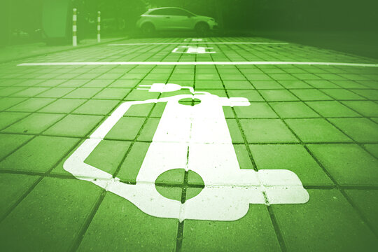Electric vehicle parking symbol with green overlay on paved urban charging area. Eco-friendly mobility concept.