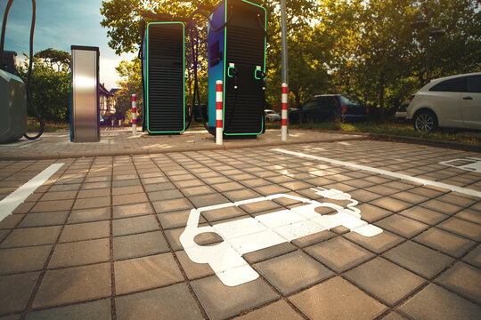 Electric vehicle parking symbol in front of modern charging stations in warm afternoon light. Urban clean energy concept.