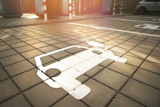 Close-up of electric vehicle parking symbol on paved charging area in warm evening light.