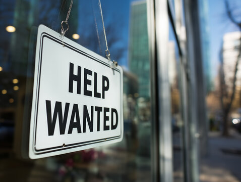 Help wanted sign hanging in a shop window indicating job openings during daytime in an urban setting
