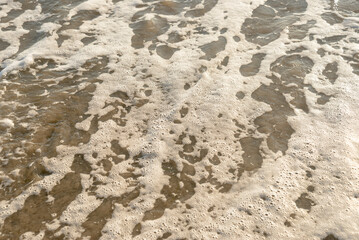 Sea foam on sandy beach surface