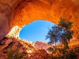 Sunlit Jacob Hamblin Arch framing a rocky canyon with a tiny hiker
