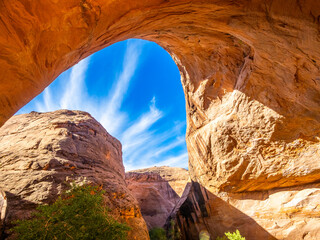 Sunlight pouring through Jacob Hamblin Arch with blue sky and streaked clouds