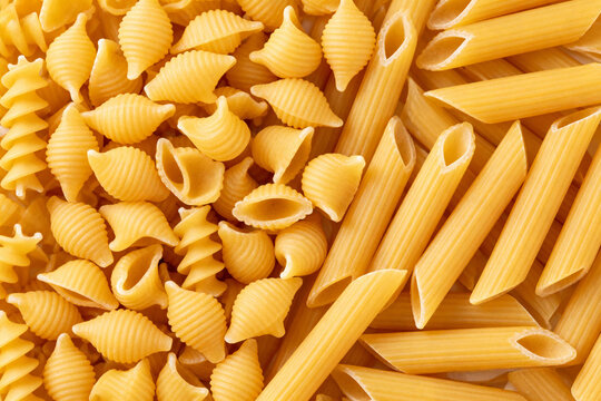 Close up shot of various types of dry pasta including penne rigate and conchiglie arranged together