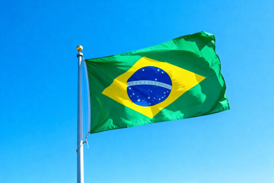 Brazilian flag waving against a clear blue sky on a metal pole with a golden ball on top of the pole - Powered by Adobe