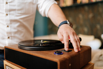 Close up hand lowering tonearm onto vinyl record on wooden turntable at home