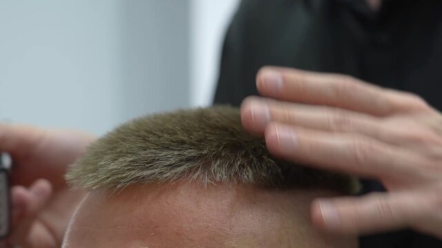 A skilled hairdresser carefully trims the top of a man's hair using clippers in a stylish barbershop setting. The man appears relaxed and confident, embracing a fresh look