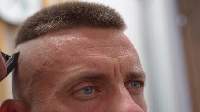 A man is getting a trendy haircut at a barbershop. The barber carefully trims the hair using clippers, focusing on creating a clean and stylish look.