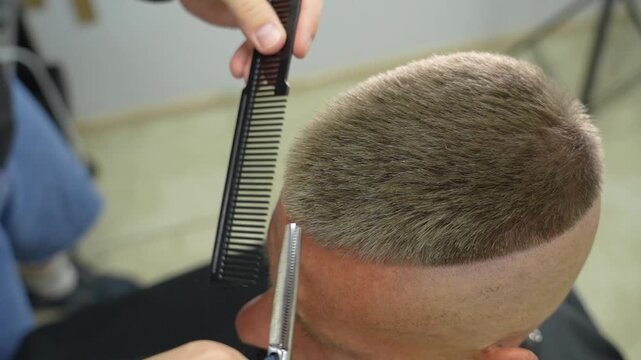 A barber uses a comb and scissors to cut a man's hair in a barbershop. The man with a beard is receiving a haircut from the barber. The goal is to give him a fresh, new hairstyle