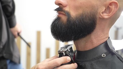 Man's beard is carefully combed, trimmed and shaped at a modern barbershop. The barber skillfully uses scissors and a comb to create an elegant look on a busy day