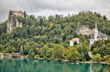 Fototapeta premium Lake Bled, Slovenia – July 22, 2025: Panoramic view of Bled Castle and St. Martin’s Church overlooking the turquoise lake and island from a nearby terrace. 